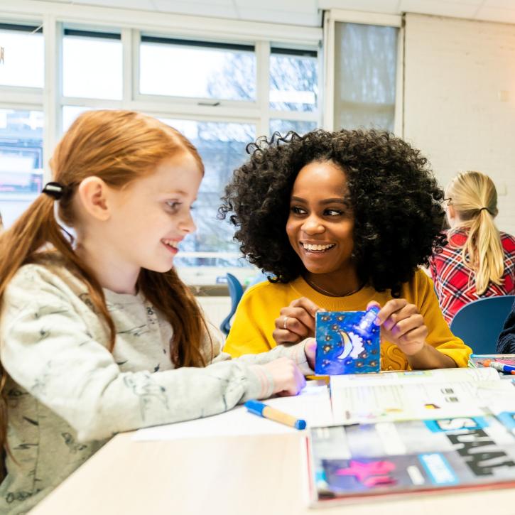 leerkracht en leerling zitten samen lachend aan tafeltje