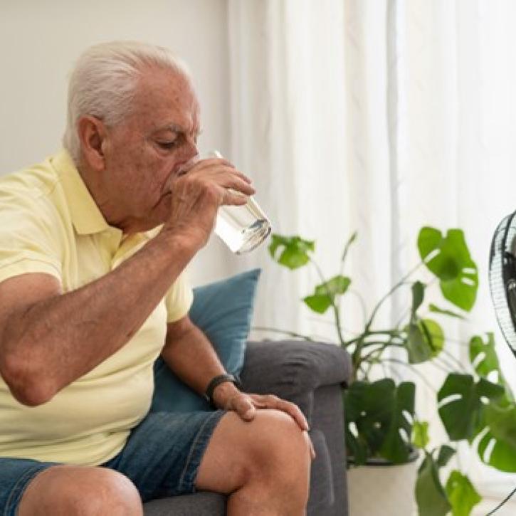 oudere man drinkt water in de hitte binnenshuis