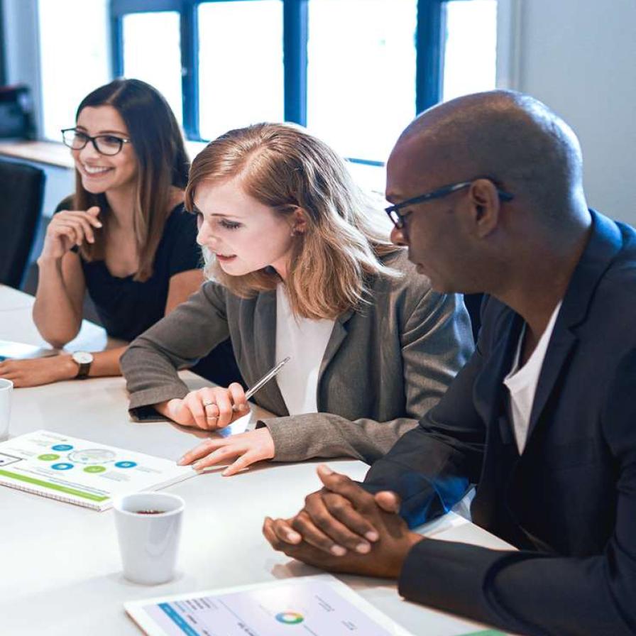 drie mensen buigen zich aan een vergadertafel over verschillede documenten
